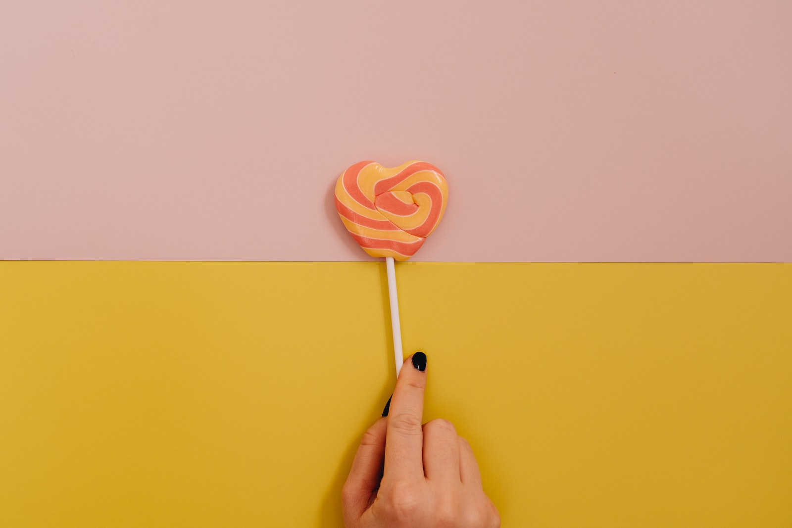Woman Hand Holding Lollipop on Two Colored Background